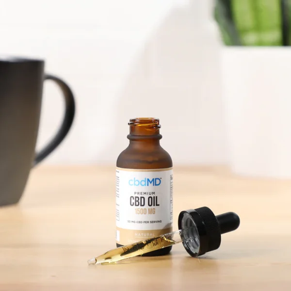CBDMD 1500mg CBD Tincture bottle sitting on a wooden table, with a dropper filled with CBD oil positioned in front of it.