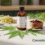 A brown glass bottle with a white label sits on a countertop surrounded by assorted herbs, including lavender, chamomile, rosemary, and cannabis leaves. A small wooden bowl filled with dried red berries is nearby, and the words “Cannabis Pharmacy” appear in green text in the lower right corner.